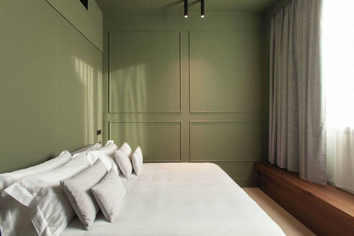 Un dormitorio con una cama grande, una ventana con cortinas y una pared verde.