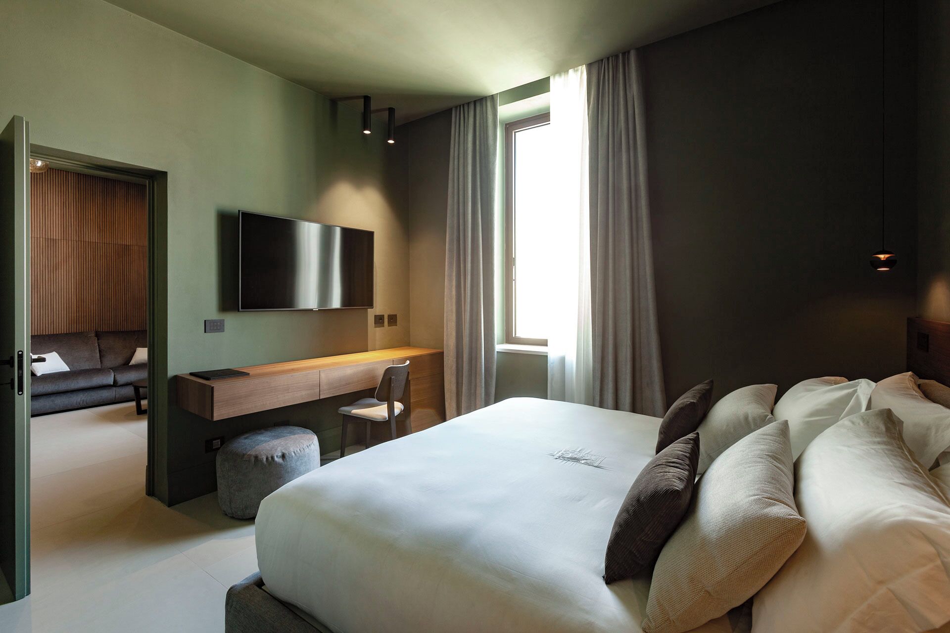 Habitación de hotel moderna con una cama grande, un escritorio, una silla, un televisor de pantalla plana y un ventanal con cortinas.