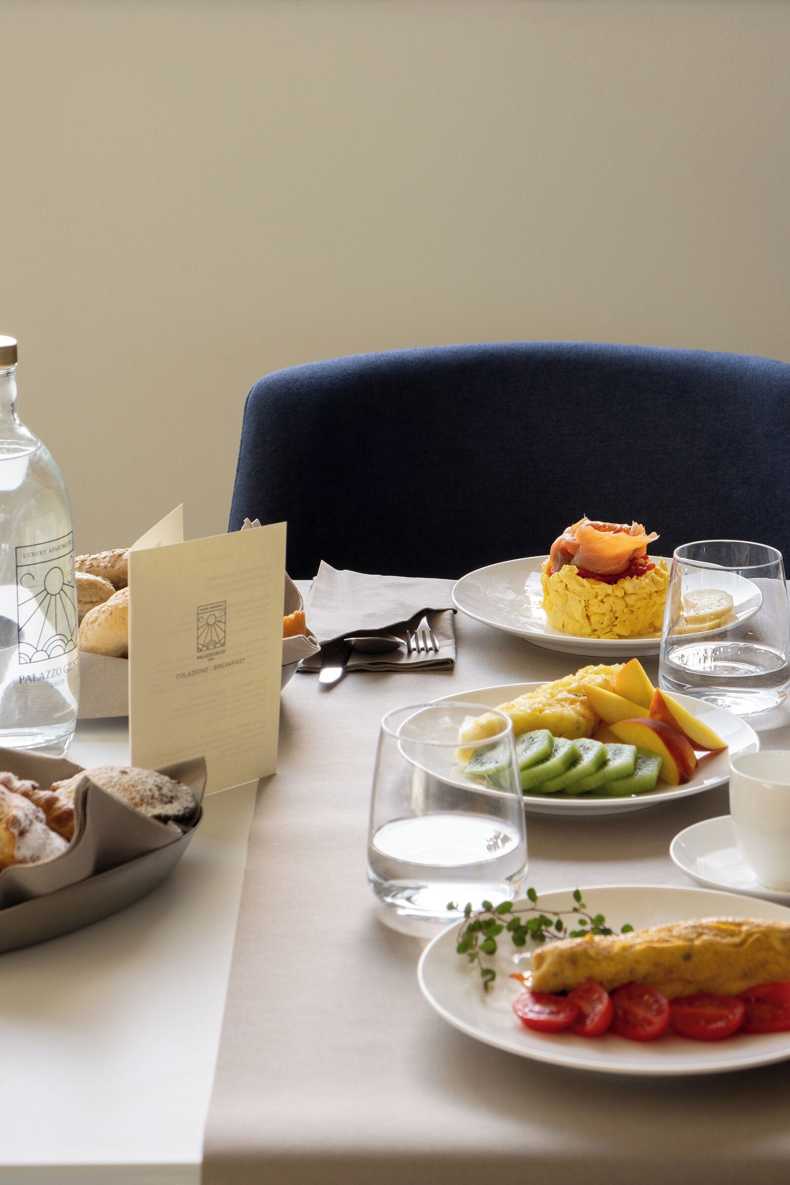 A breakfast setting with a plate of scrambled eggs, a slice of ham, and a glass of water on a table.