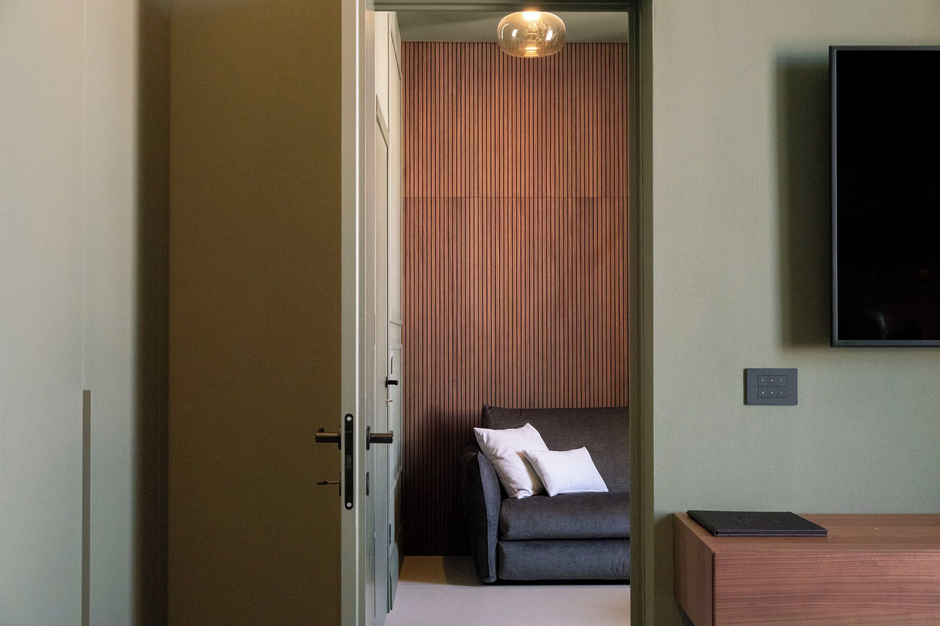 A modern hotel room with a sofa, a TV, and a wooden panel wall.
