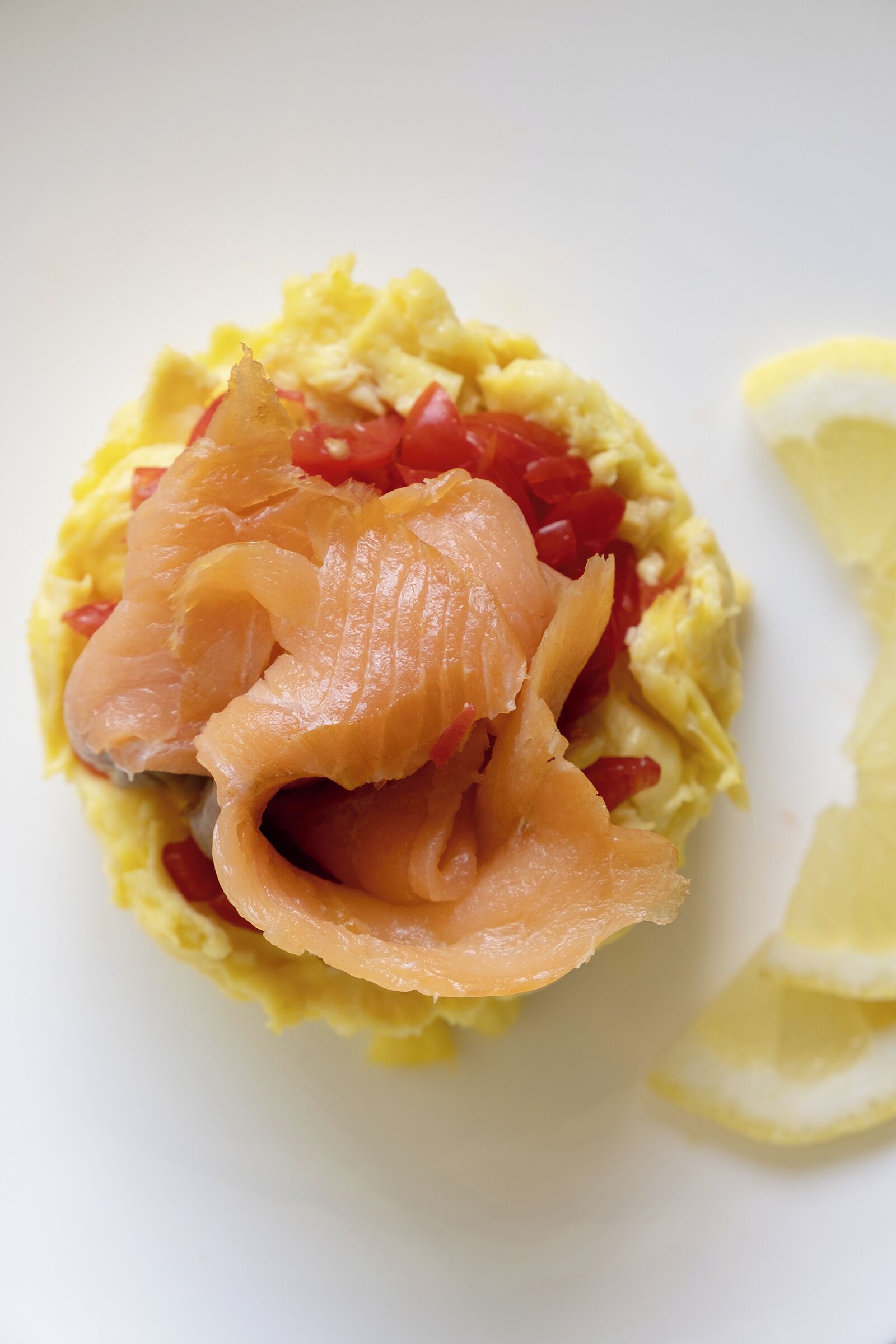 A dish with scrambled eggs, smoked salmon, and red bell peppers.