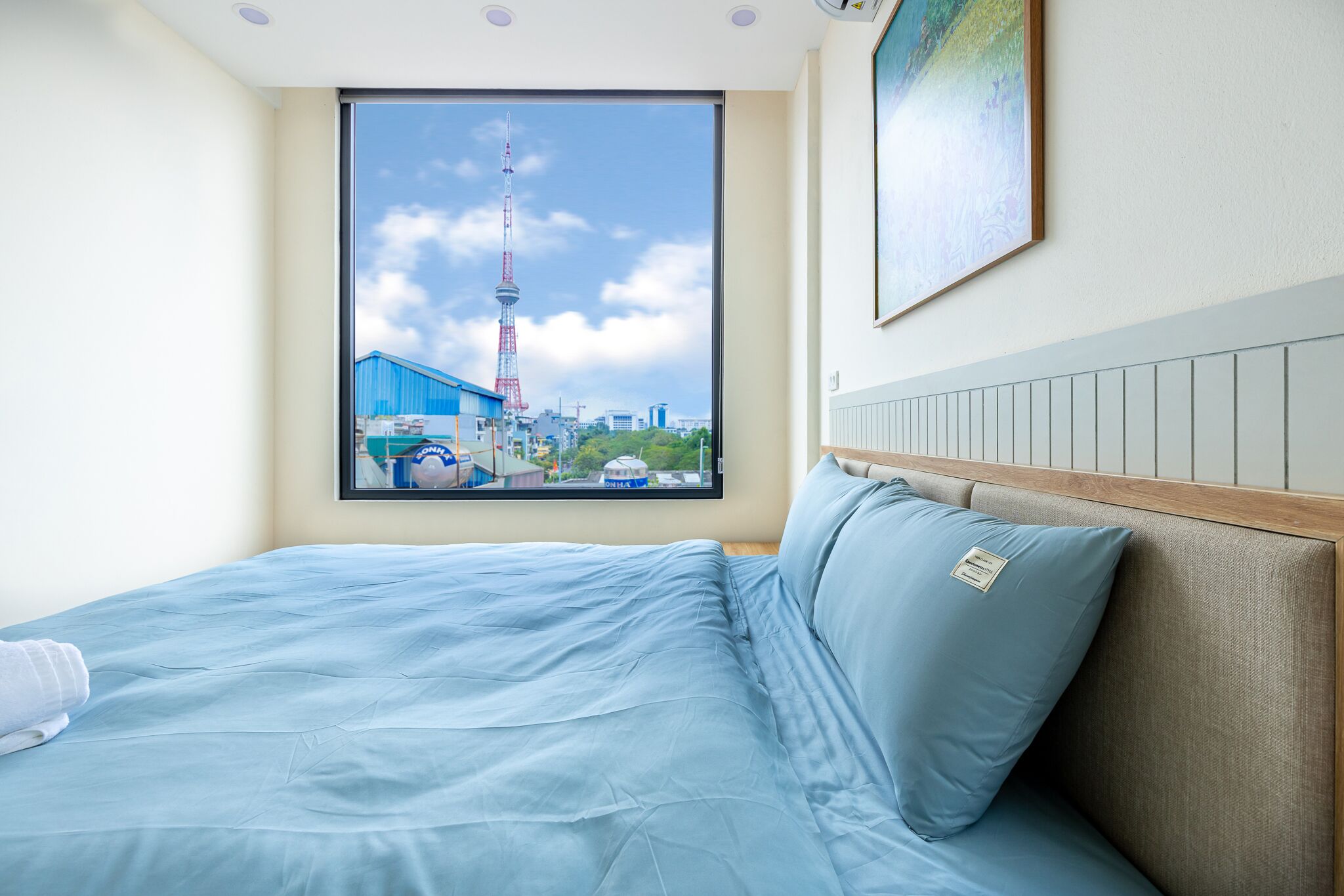 Une chambre d’hôtel dotée d’une grande fenêtre donnant sur un paysage urbain, avec notamment une tour imposante.