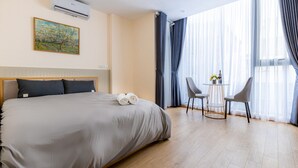 Una habitació d'hotel amb un llit gran, una taula rodona petita amb dues cadires, un quadre a la paret i una finestra amb cortines primes.