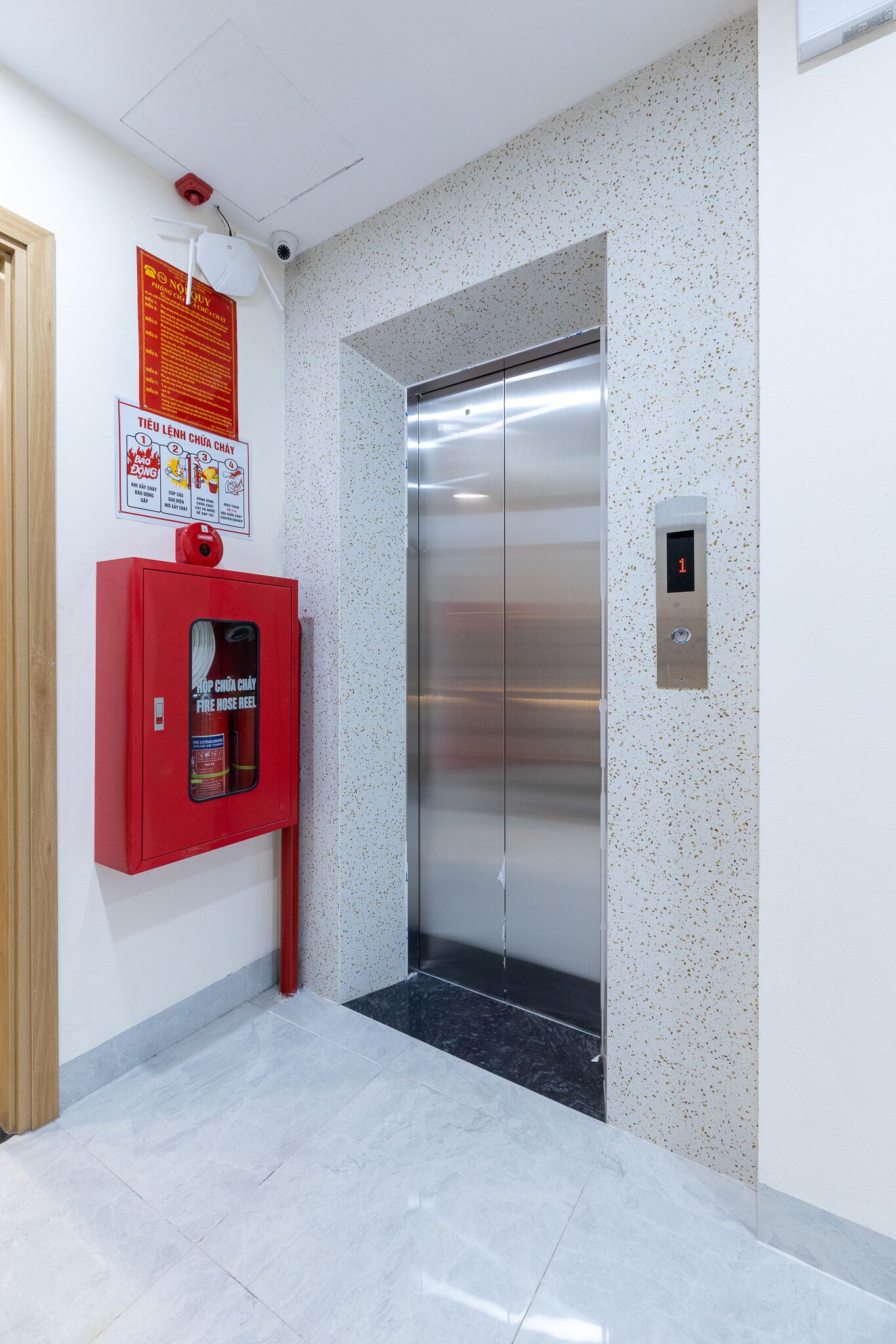 An elevator with a digital display, a fire extinguisher, and a fire safety poster on the wall.