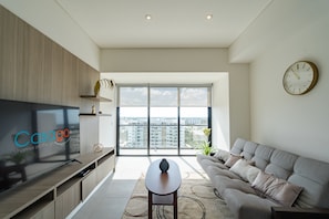 A modern living room with a large TV, a sofa, a coffee table, and a view of the city through large windows. - Tower Indico by Casago (Mérida)