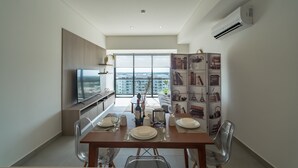A modern dining area with a large window, a flat-screen TV, and a decorative cabinet with various items. - Tower Indico by Casago (Mérida)