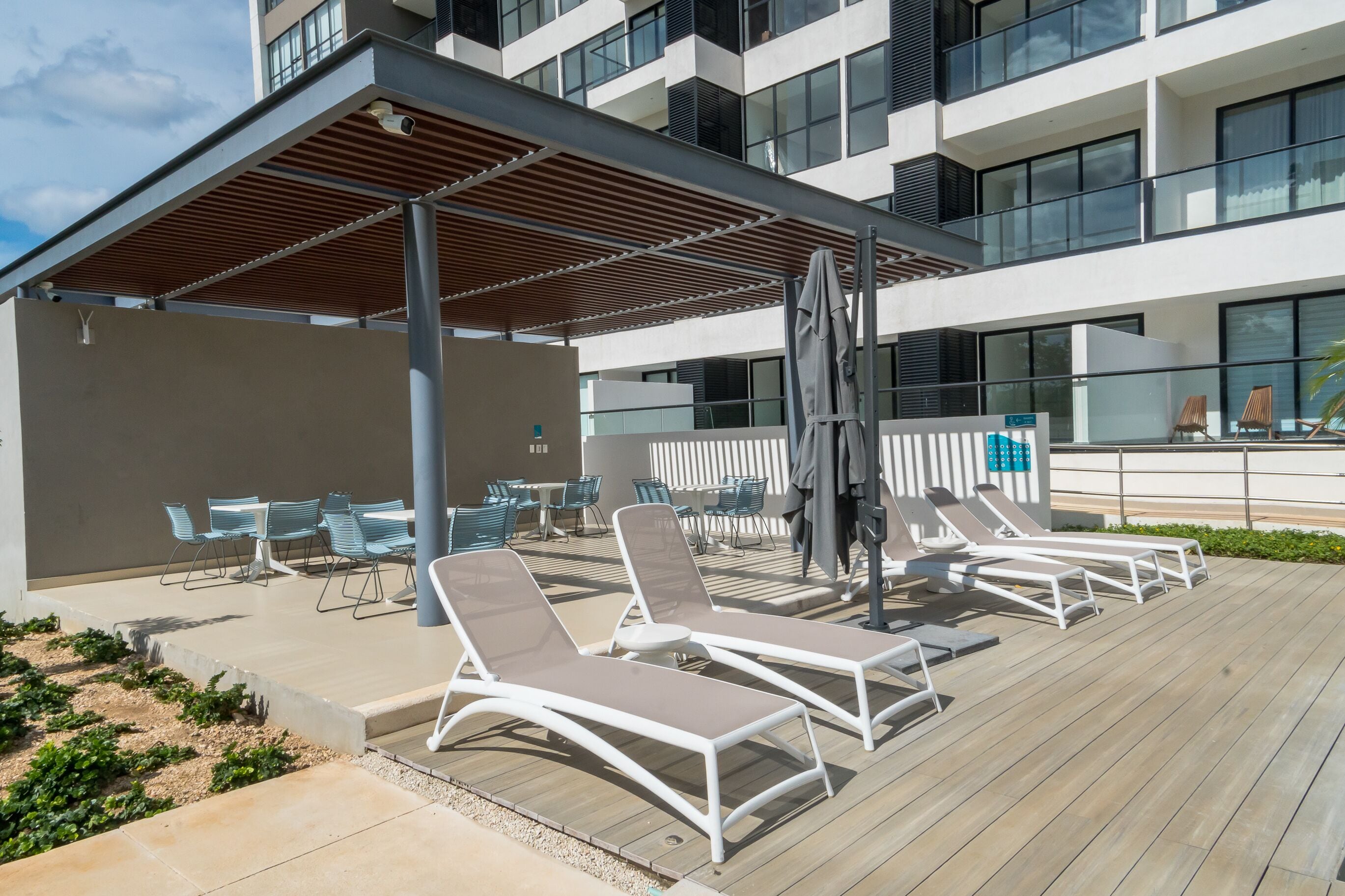 A rooftop terrace with sun loungers, a covered seating area, and a view of a modern building.