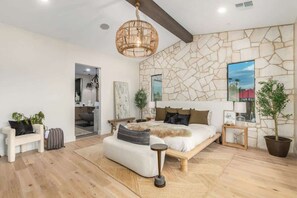 Une chambre moderne avec un mur en pierre, un grand lit, un luminaire suspendu et une vue sur l’extérieur.