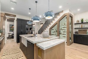 A modern kitchen with a central island, dark cabinetry, and a staircase leading to an upper level. - 6 Beds | 5 Showers | Htd. Pool, Firepit & Putt Grn (Scottsdale)