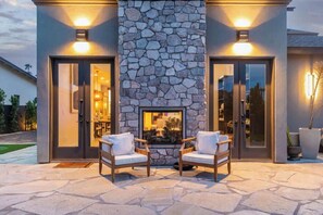A modern building with a stone fireplace, two chairs, and a glass door entrance. - 6 Beds | 5 Showers | Htd. Pool, Firepit & Putt Grn (Scottsdale)