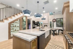 Une cuisine moderne dotée d’un îlot central, d’un escalier en bois, de luminaires suspendus et d’un coin repas offrant une vue agréable.