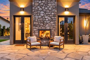 Une cheminée en pierre, deux fauteuils placés devant, un mur en pierre et deux portes avec des luminaires.