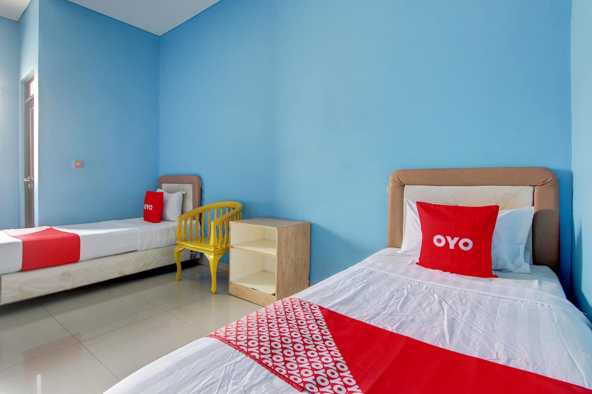 Quarto de hotel com duas camas, uma mesa de cabeceira de madeira, uma cadeira amarela e um travesseiro vermelho com a palavra "OYO".