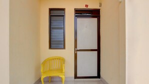 A narrow hallway with a yellow bench, a door with a number plate, and a window with horizontal bars. - Hotel O Wisma Subur Syariah (Pekalongan)