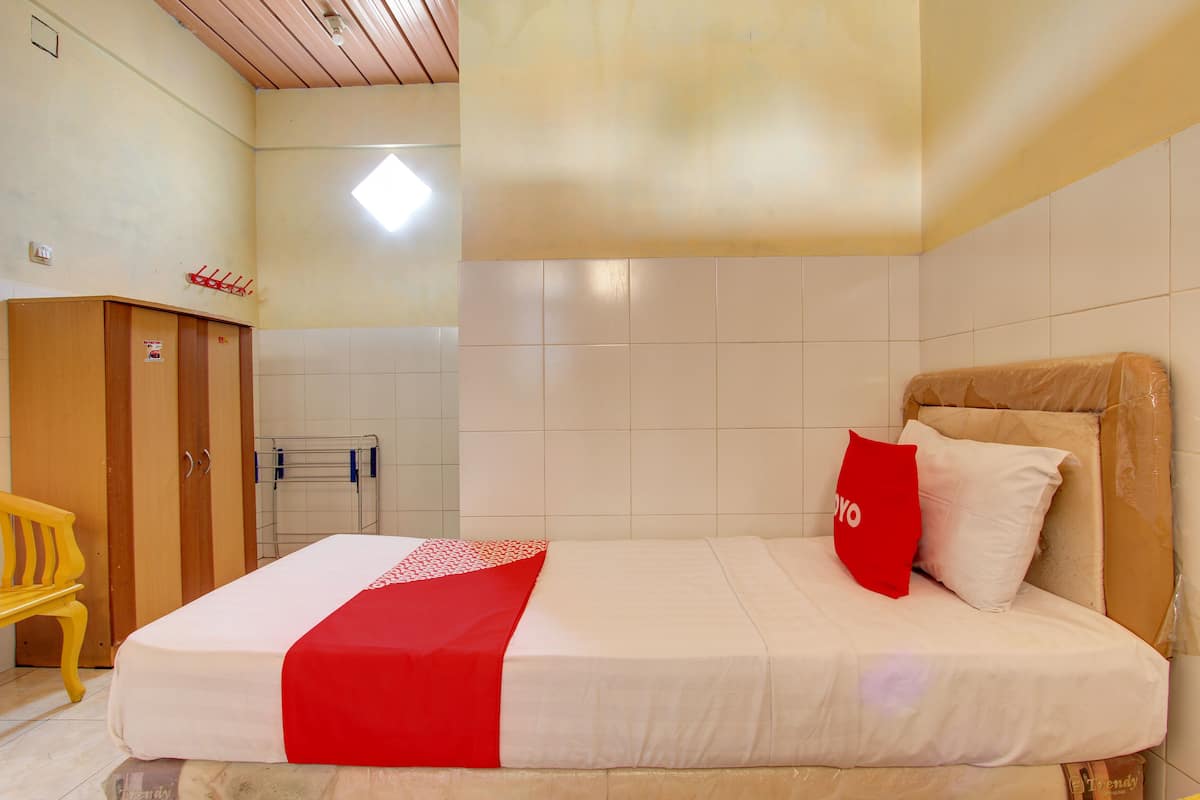 Quarto de hotel com cama, guarda-roupa de madeira, um banco e um porta-toalhas.