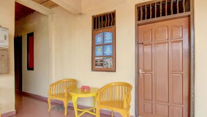 A hallway with a wooden door, a bulletin board with hotel information, and two yellow chairs and a small table. - Hotel O Wisma Subur Syariah (Pekalongan)