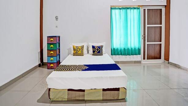 A neatly arranged bedroom with a bed, a dresser, a window with curtains, and a door. - Hotel O Wisma Subur Syariah (Pekalongan)