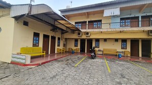 A courtyard with hexagonal paving, yellow benches, and a motorcycle parked. - Hotel O Wisma Subur Syariah (Pekalongan)