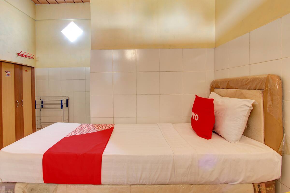 Quarto de hotel com uma cama, um guarda-roupa de madeira e uma parede revestida em azulejos.