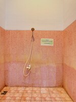 Zona de ducha con azulejos rosas, un cabezal de ducha y un cartel con texto.