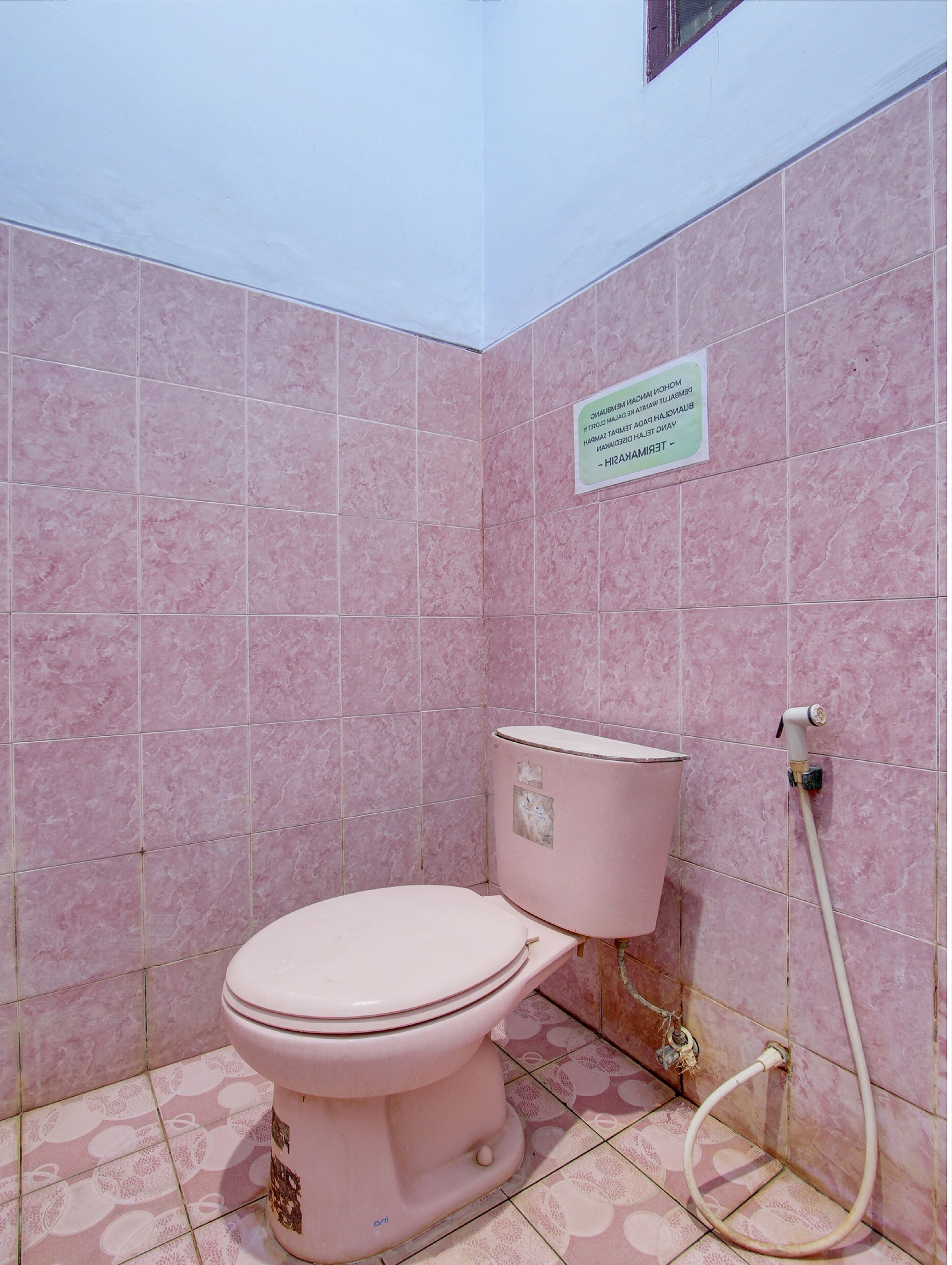 Baño con azulejos y retrete rosados, y un conducto de agua visible.