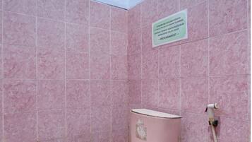 Baño con azulejos y retrete rosados, y un conducto de agua visible.