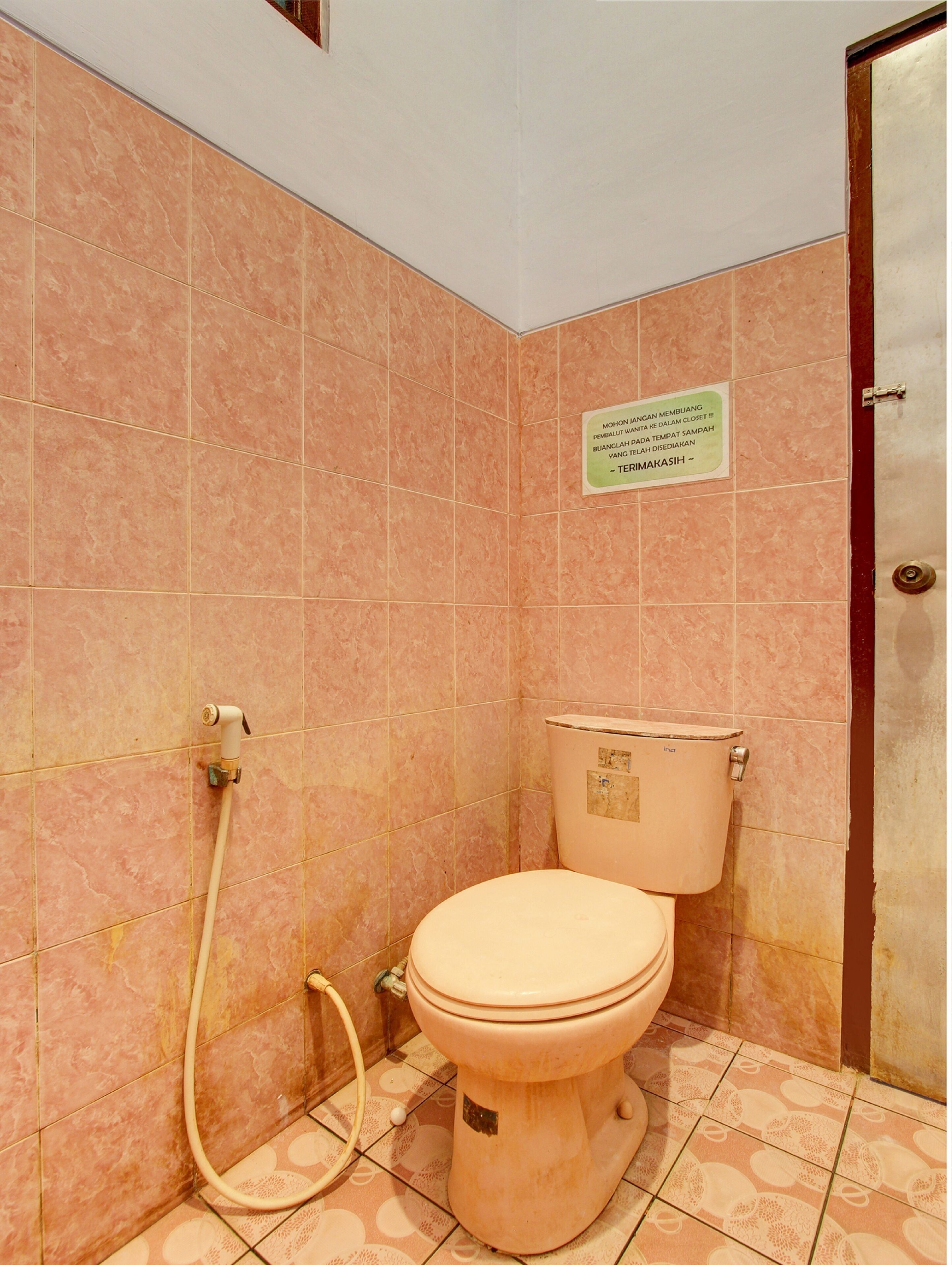 A bathroom with pink tiles, a toilet, and a shower hose.