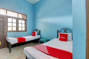 Habitación con dos camas individuales, cada una con almohada roja y edredón blanco. Hay un taburete pequeño y una ventana con vista a edificios.
