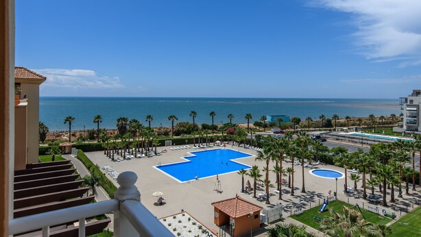 Resort com uma piscina grande, palmeiras e vista para o mar.