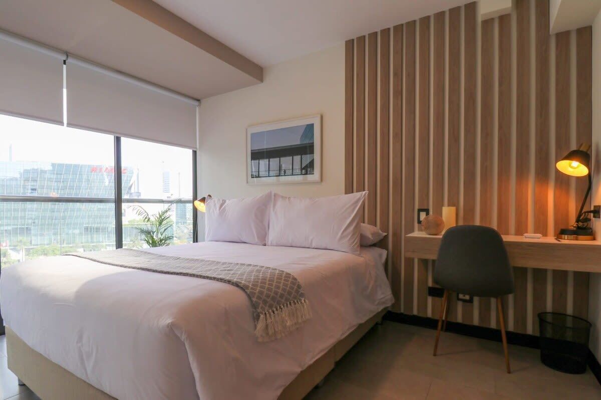 Une chambre d’hôtel avec un grand lit, un bureau avec une chaise, une vue sur la ville et un mur revêtu de panneaux en bois.