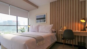 Habitación de hotel con una cama grande, un escritorio con silla, vista a la ciudad y un panel de pared de madera.