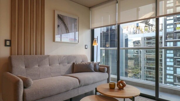 Una sala de estar moderna con un sofá, una mesa redonda de centro y un ventanal con vistas a la ciudad.