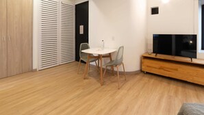 A modern, well-lit room with a wooden floor, a round dining table with two chairs, a TV on a wooden stand, and a sliding door closet. - w* | Cozy Loft in Laureles (Medellín)