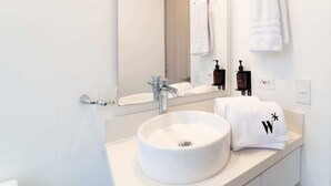 A modern bathroom with a round white sink, a mirror, and two towels hanging on hooks. - w* | Cozy Loft in Laureles (Medellín)