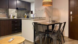 Cocina compacta con armarios oscuros, encimera de granito y una isla central con lavamanos. Hay un comedor con mesa y sillas, y una lámpara colgante sobre la isla.