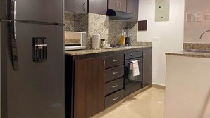 Una cocina moderna con armarios oscuros, horno empotrado, cafetera y microondas.