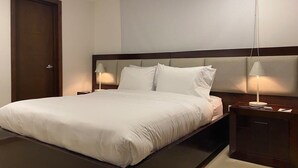 Una habitación de hotel con una cama grande, un cabecero de madera, dos mesitas de noche con lámparas y una puerta.