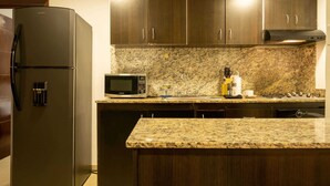 Eine Küche mit dunklen Holzausziehtüren, einem schwarzen Kühlschrank, einer Mikrowelle und Granit Arbeitsplatten.