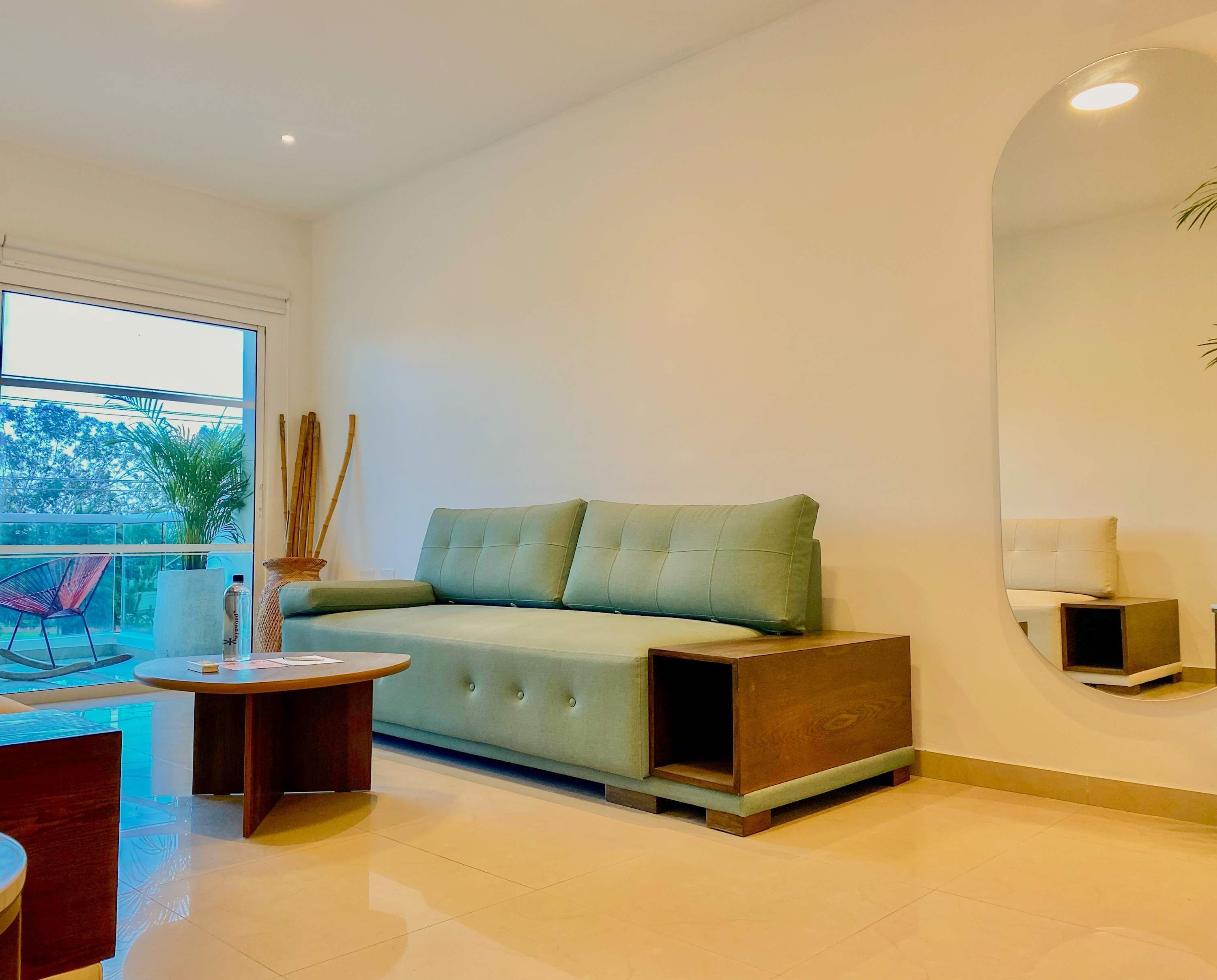 Una sala de estar moderna con un sofá verde claro, una mesita redonda de madera y un espejo grande en la pared.