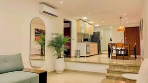 A modern living room with a sofa, a coffee table, and a dining area with a table and chairs. There is a kitchen in the background with a refrigerator and a microwave. - w*| Spectacular 2BR w/ Balcony n AC in Bocagrande (Cartagena de Indias)