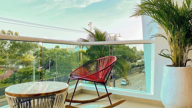 A balcony with a rocking chair, a small round table, and a potted plant. - w*| Spectacular 2BR w/ Balcony n AC in Bocagrande (Cartagena de Indias)