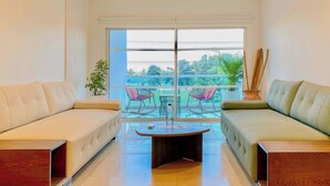 A modern living room with two sofas, a coffee table, and a large window with a view of greenery and a building labeled "BOLIVIA". - w*| Spectacular 2BR w/ Balcony n AC in Bocagrande (Cartagena de Indias)