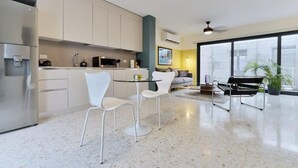 Una cocina moderna con armarios blancos, un refrigerador de acero inoxidable y un comedor con sillas blancas y una mesa de vidrio.