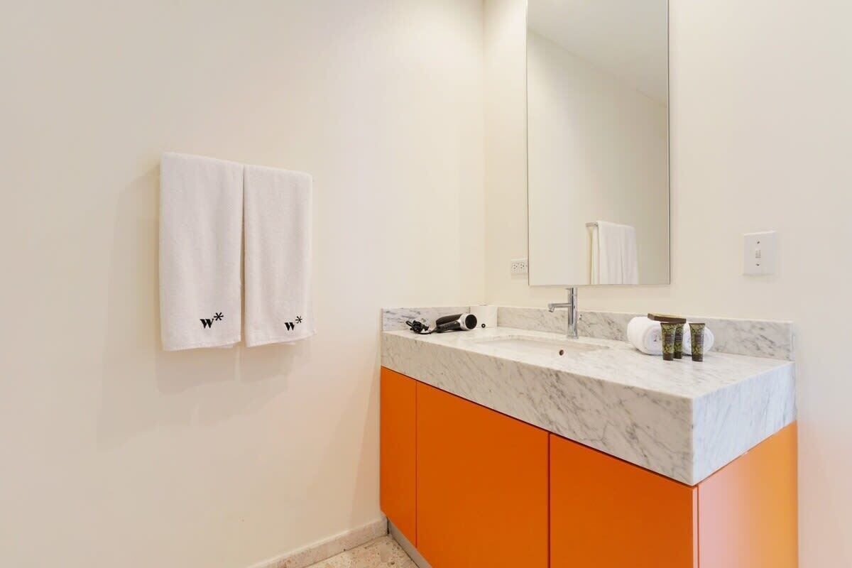 Ein Badezimmer mit einem weißen Waschbecken, orangefarbenen Schränken und zwei weißen Handtüchern an der Wand.