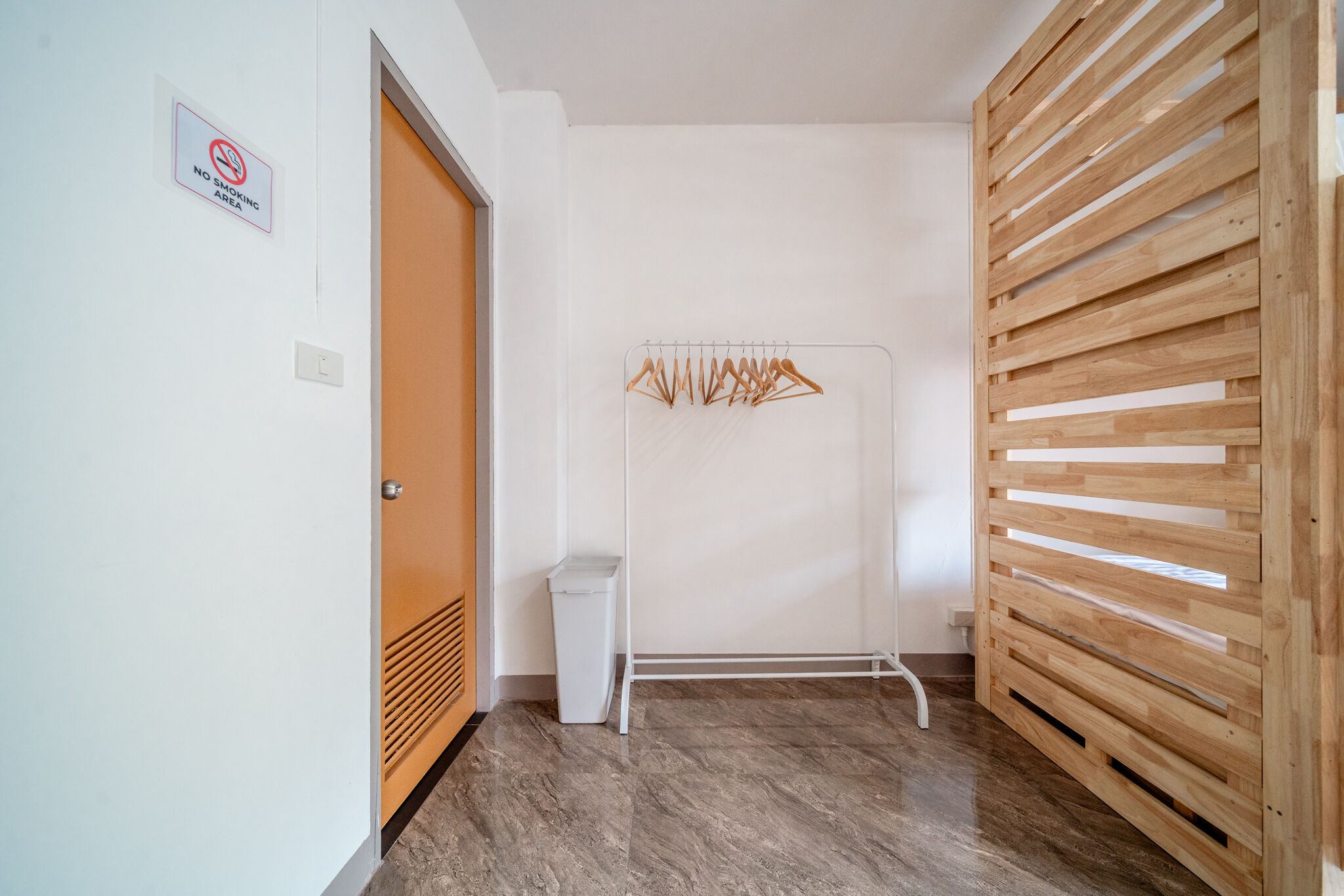 A hallway with a no-smoking sign, a coat rack, a trash bin, and a wooden slatted partition.