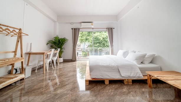 Quarto moderno com cama, escrivaninha de madeira, cadeira, cabideiro e planta em vaso.