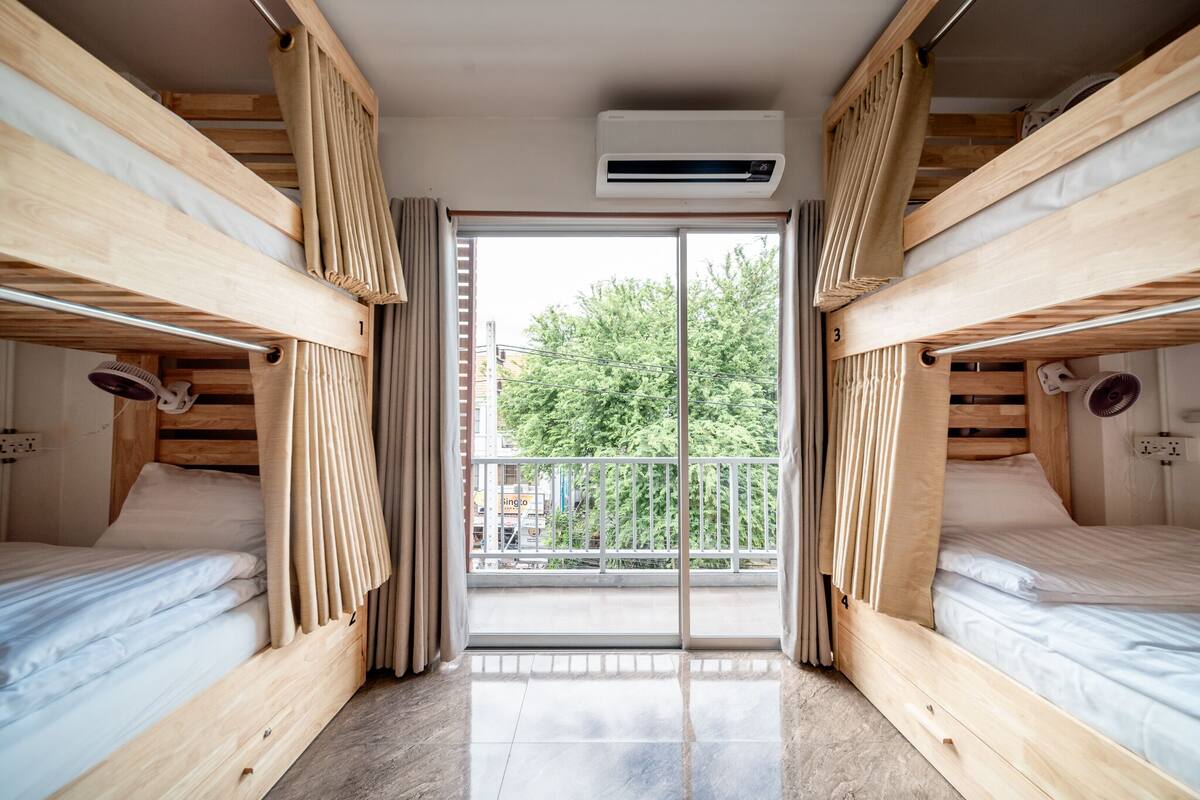 A room with two bunk beds, a sliding glass door to a balcony, and an air conditioning unit above the door.