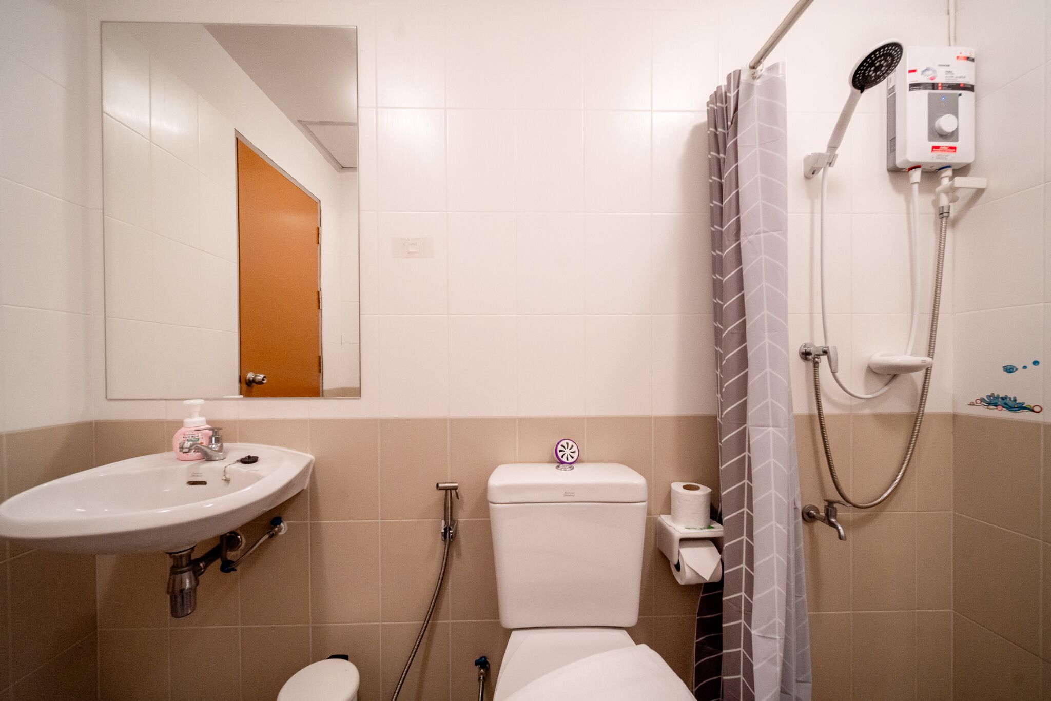 Et badeværelse med vask, toilet, bruser og spejl.
