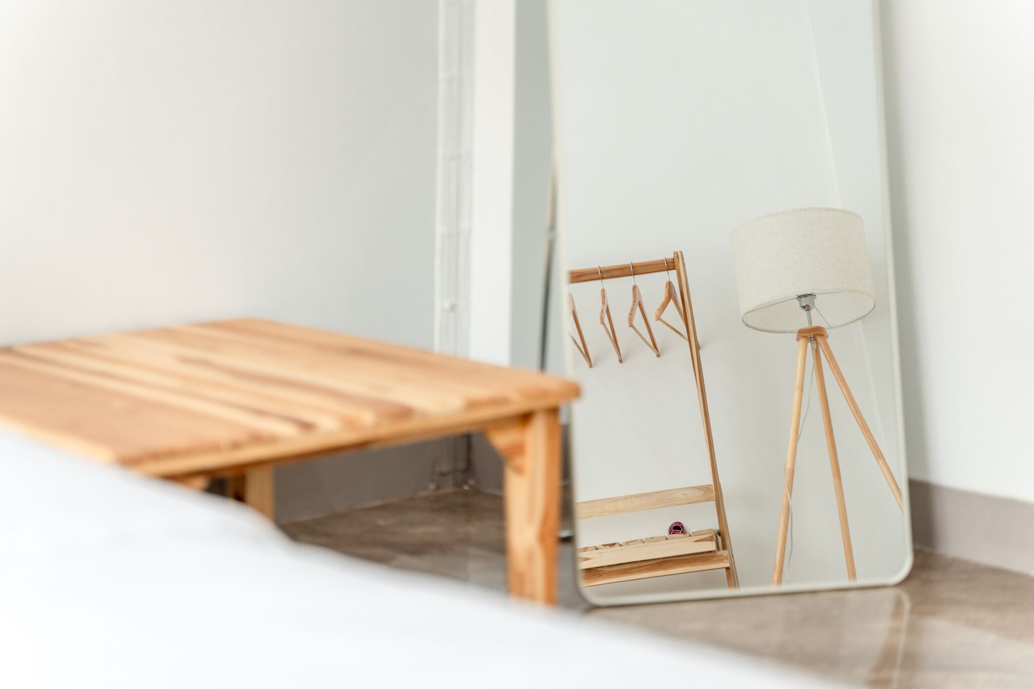 A minimalist room with a wooden bench, a mirror reflecting a lamp and a chair, and a white wall.