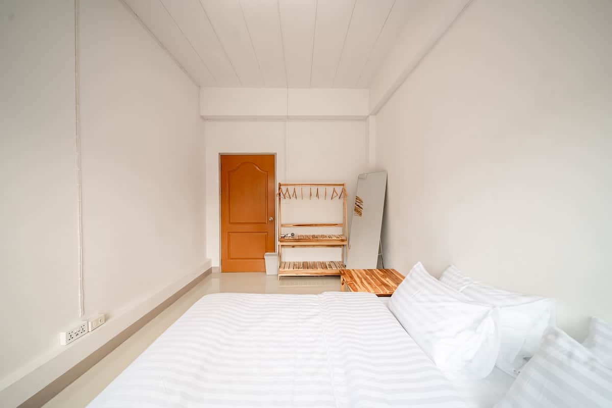 A bedroom with a bed, a wooden wardrobe, a mirror, and a door.